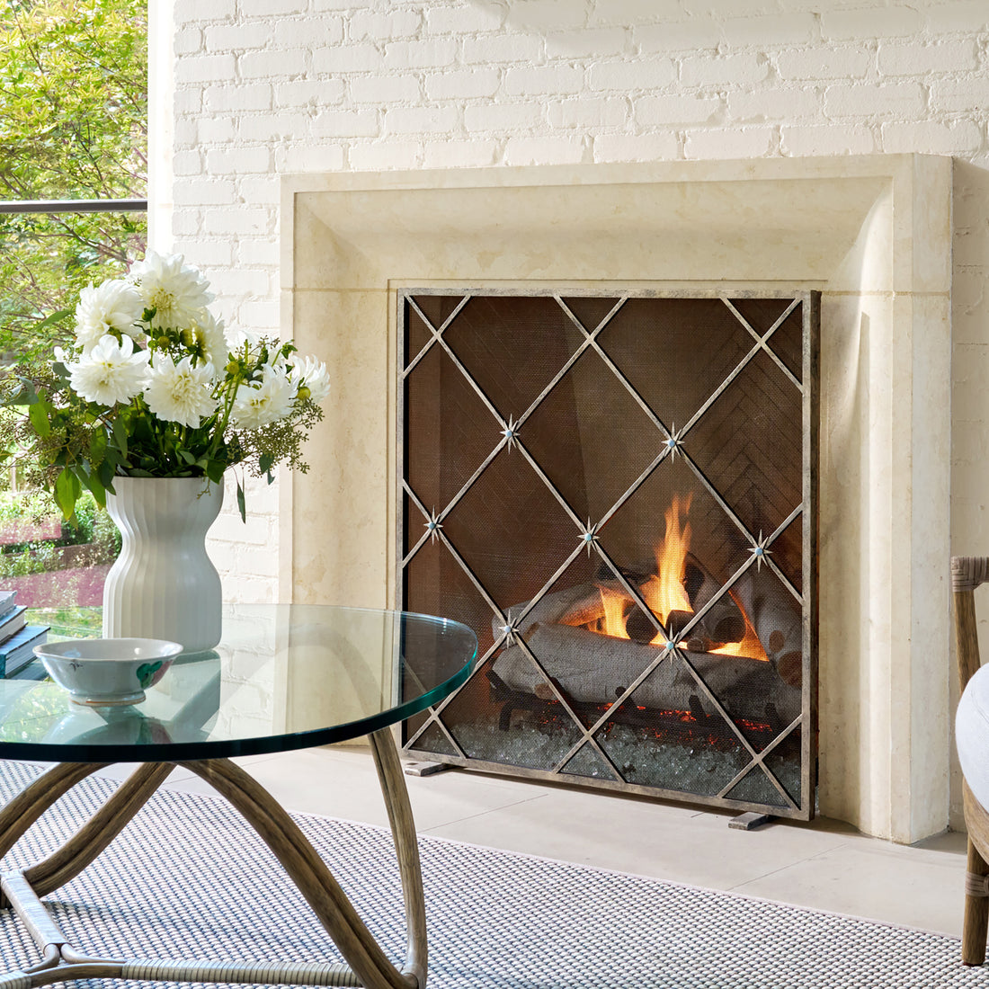 Hand-forged Celeste fireplace screen in aged silver with star accents glowing beside an active fire.