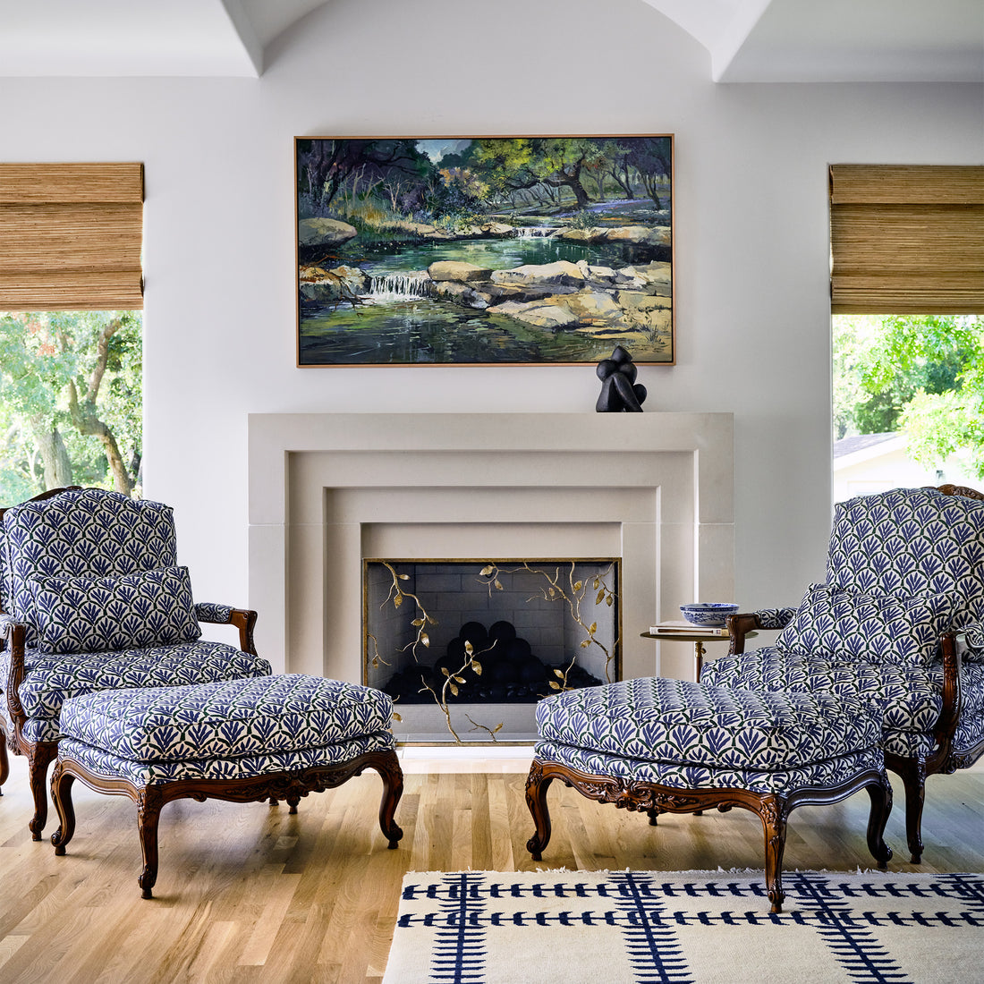 Fireplace in elegant living room with a luxury gold branch fireplace screen, wooden mantel featuring an elegant sculpture and two patterned accent chairs.