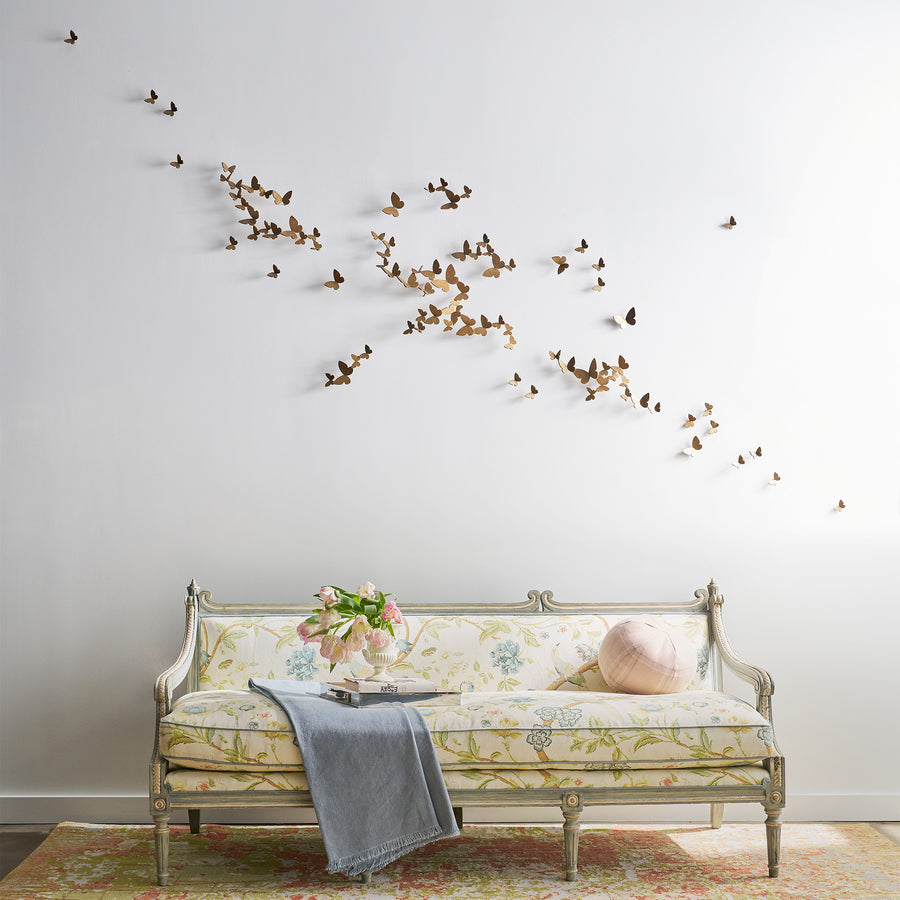 Decorative metal wall art with flying butterflies above a floral-patterned bench.
