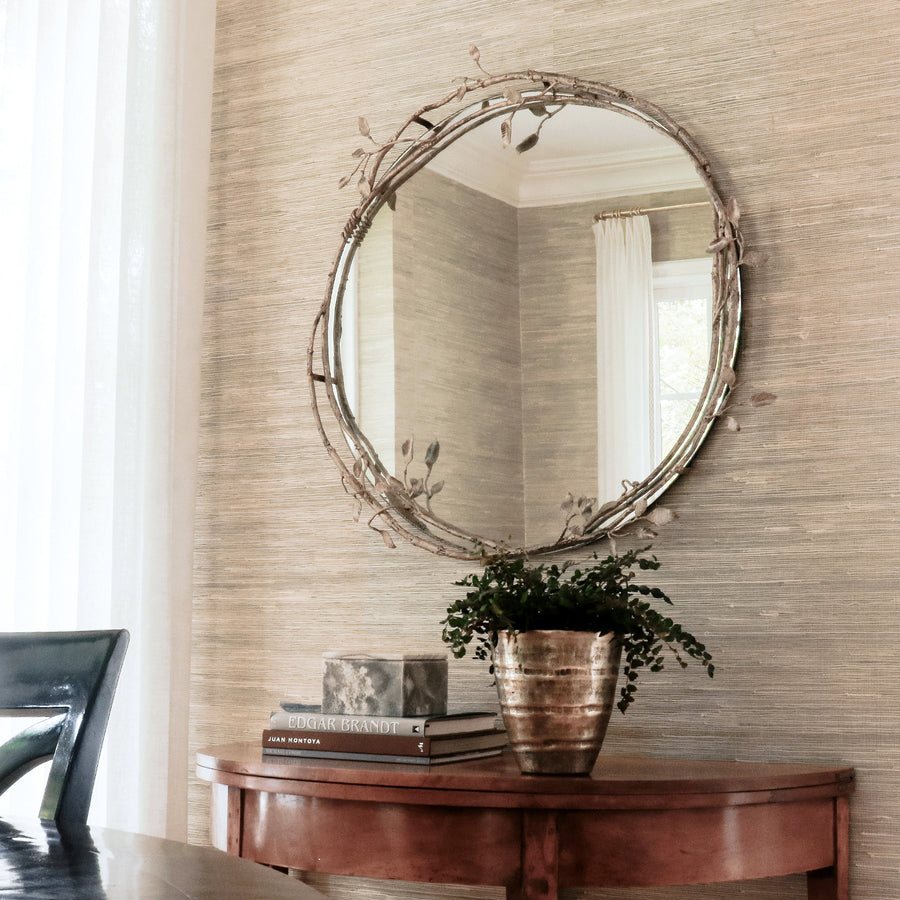Elegant lennox mirror with vine like metal frame on a textured wall, above a wooden console table holding books and a plant.