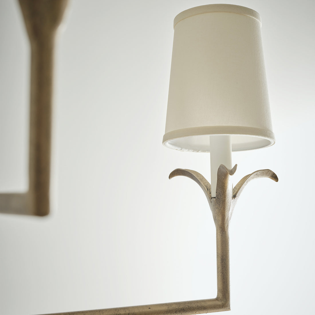 Lily stems chandelier with a tall candle shaped holder and cream fabric shade, set in a gold finish, enhancing a minimalist space.