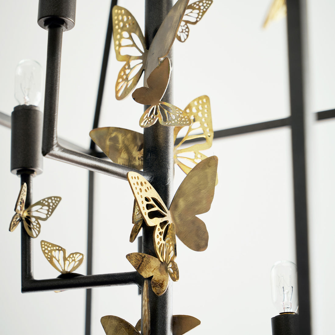 Metal butterflies in gold adorn a monarch lantern chandelier, adding an elegant and artistic touch by Claire Crowe Collection.