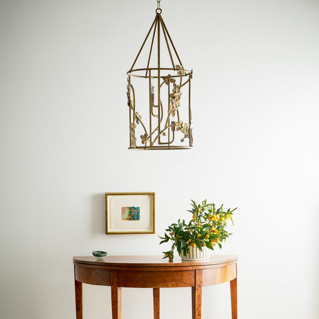 Hanging sakura lantern chandelier featuring a gold finish with floral accents and a pyramid top design sits above a minimalist console table.