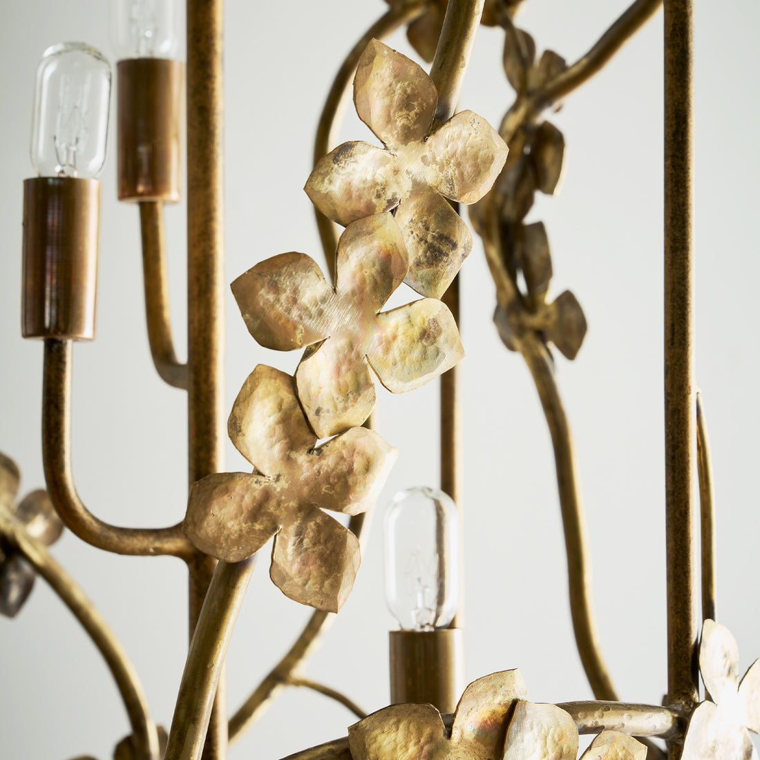 Floral detailing of an elegant sakura lantern chandelier detail with gold metallic blossoms and vertical light bulbs, set against a neutral background.