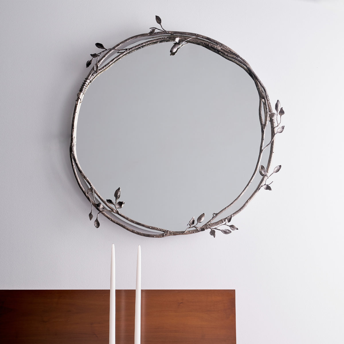 Round decorative mirror with leaf-like designs on a plain wall.