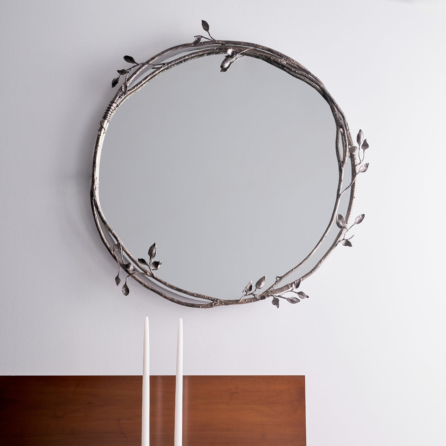 Round decorative mirror with leaf-like designs on a plain wall.
